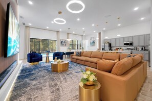 A modern living room with a large TV, a sofa, a coffee table, and a dining area. - Luxury Resort Estate Near Disney, Convention Center,  ESPN Wide World of Sports (Orlando)