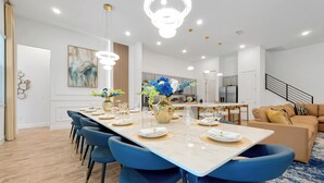 Un espace de salle à manger moderne avec une longue table, des chaises bleues et un lustre.