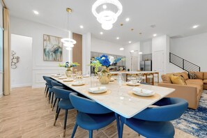 A modern dining area with a long table, blue chairs, and a chandelier. - Luxury Resort Estate Near Disney, Convention Center,  ESPN Wide World of Sports (Orlando)