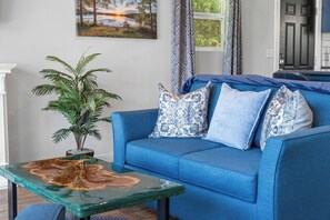A blue sofa with patterned pillows, a glass coffee table with a leaf design, and a potted plant. - Table Rock Lakefront Studio w Access_Private Hot Tub_Free Daily Tickets (Hollister)