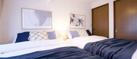 A hotel room with a bed, a wall-mounted air conditioner, two framed pictures, a wooden door, and a hanging light fixture.