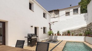 Eine Terrasse mit Pool, Grill und Gartenmöbeln.