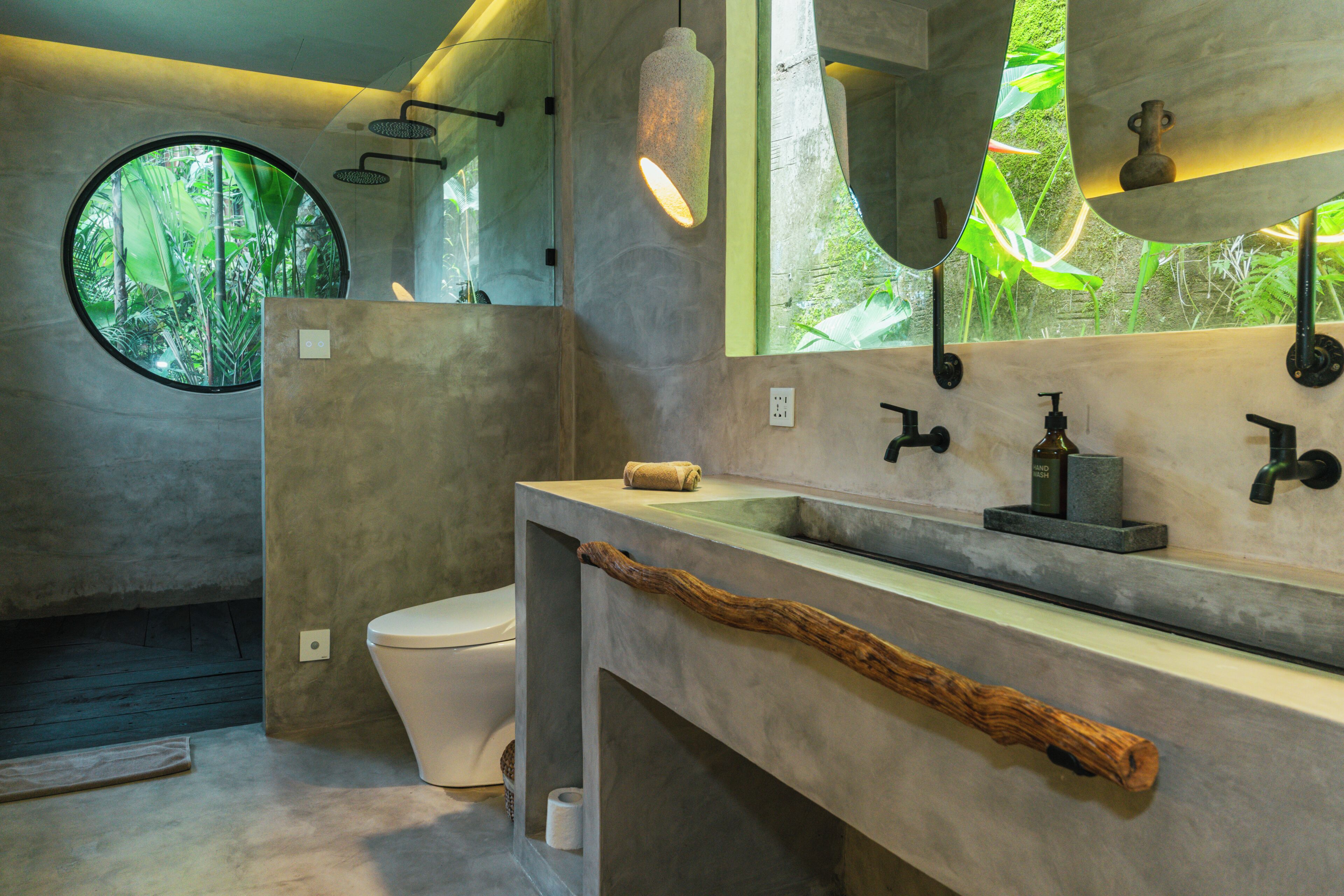 Une salle de bain moderne avec une fenêtre ronde, des toilettes et un meuble-lavabo doté d’une poignée en bois.