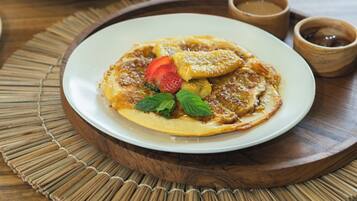 A dining table with a plate of pancakes topped with strawberries and mint, a purple drink, and a small wooden bowl.
