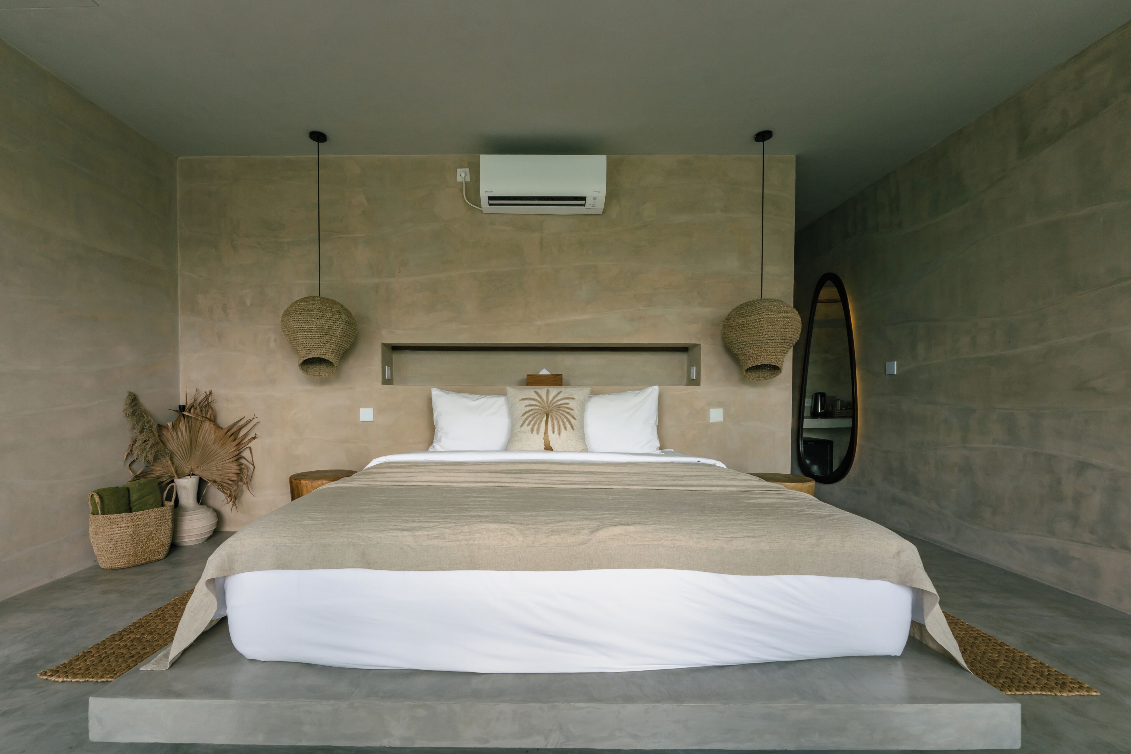 A modern bedroom with a large bed, an air conditioning unit, a wall-mounted mirror, and a woven lamp.