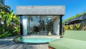 Un área de piscina moderna al aire libre con cerramiento de vidrio, terraza de madera y sofá verde.