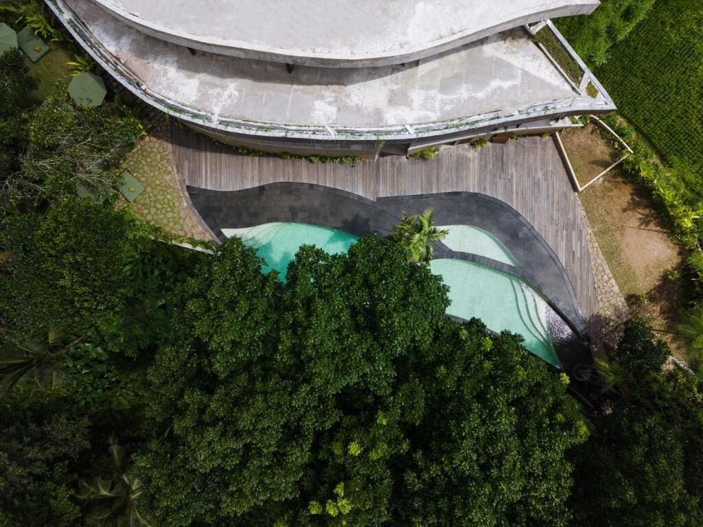An aerial view of a resort with a swimming pool, a wooden deck, and lush greenery.