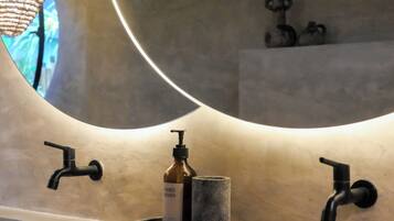 A modern bathroom with a curved mirror, two black faucets, and a hand soap dispenser on a marble countertop.
