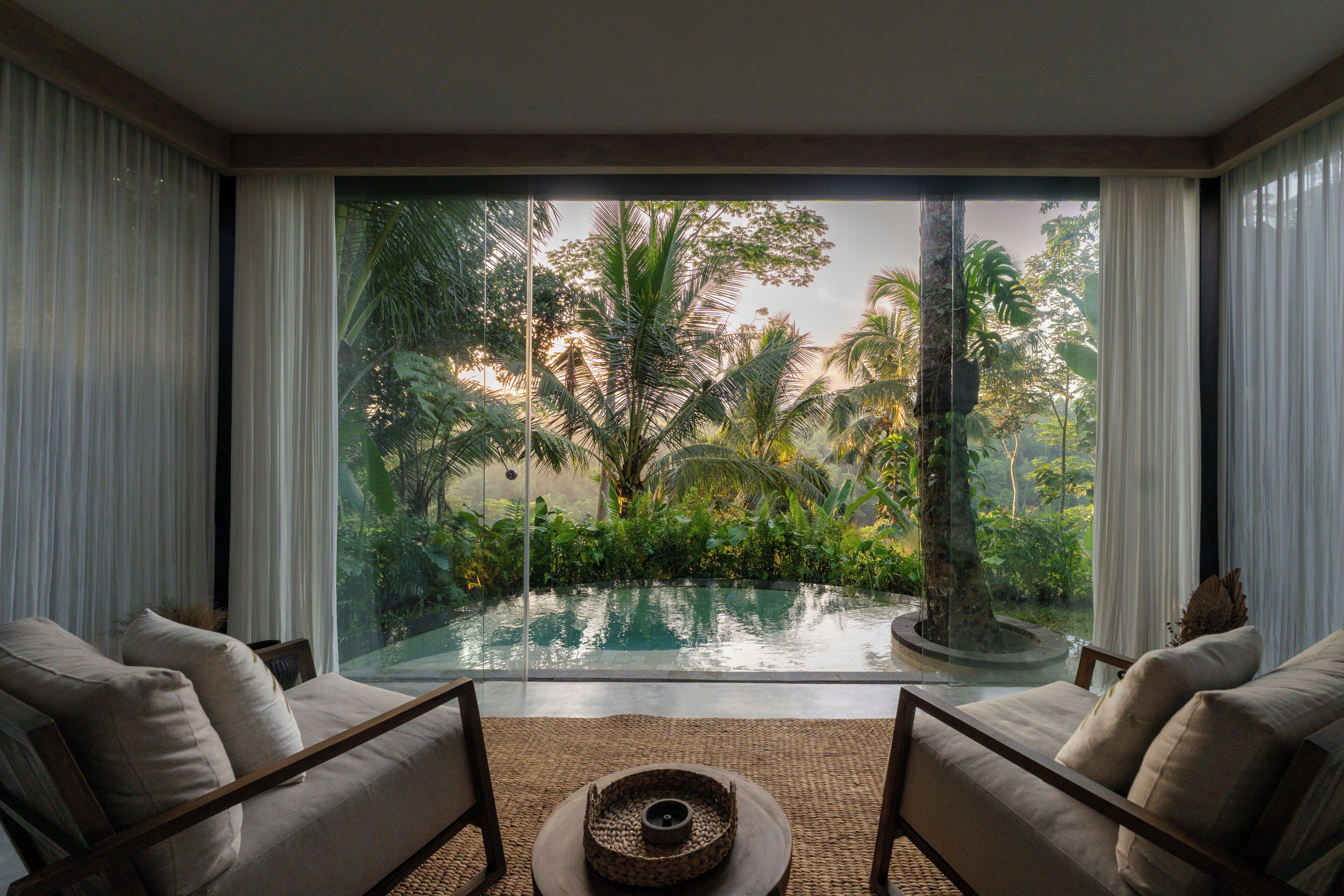 A room with a large window overlooking a pool and lush greenery.