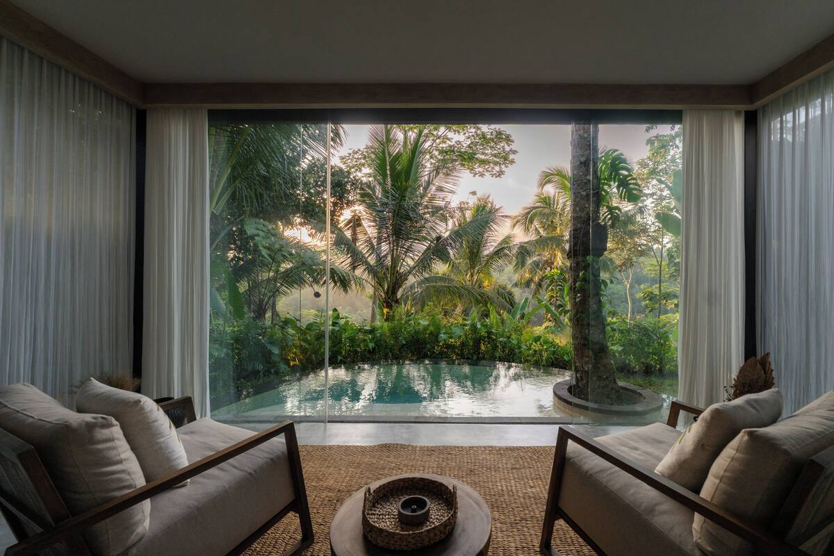 Una habitación con un amplio ventanal que da a una piscina y abundante vegetación.