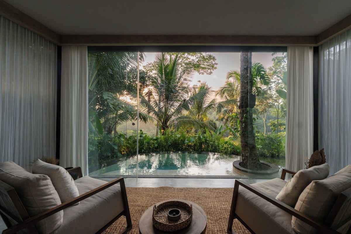 A room with a large window overlooking a pool and lush greenery.
