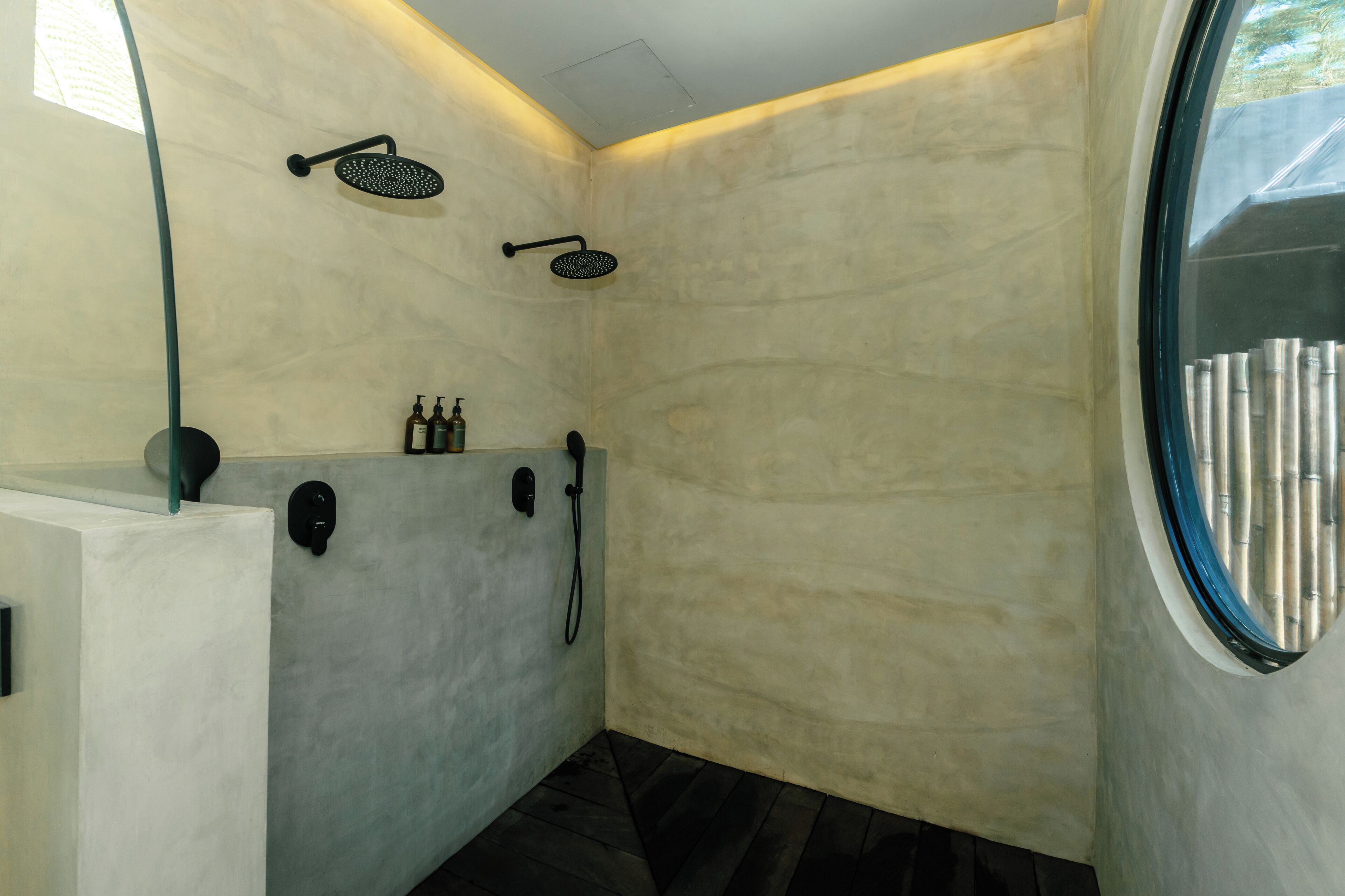 Un baño moderno con un espejo grande, una ducha con cabezal de ducha manual y un inodoro.