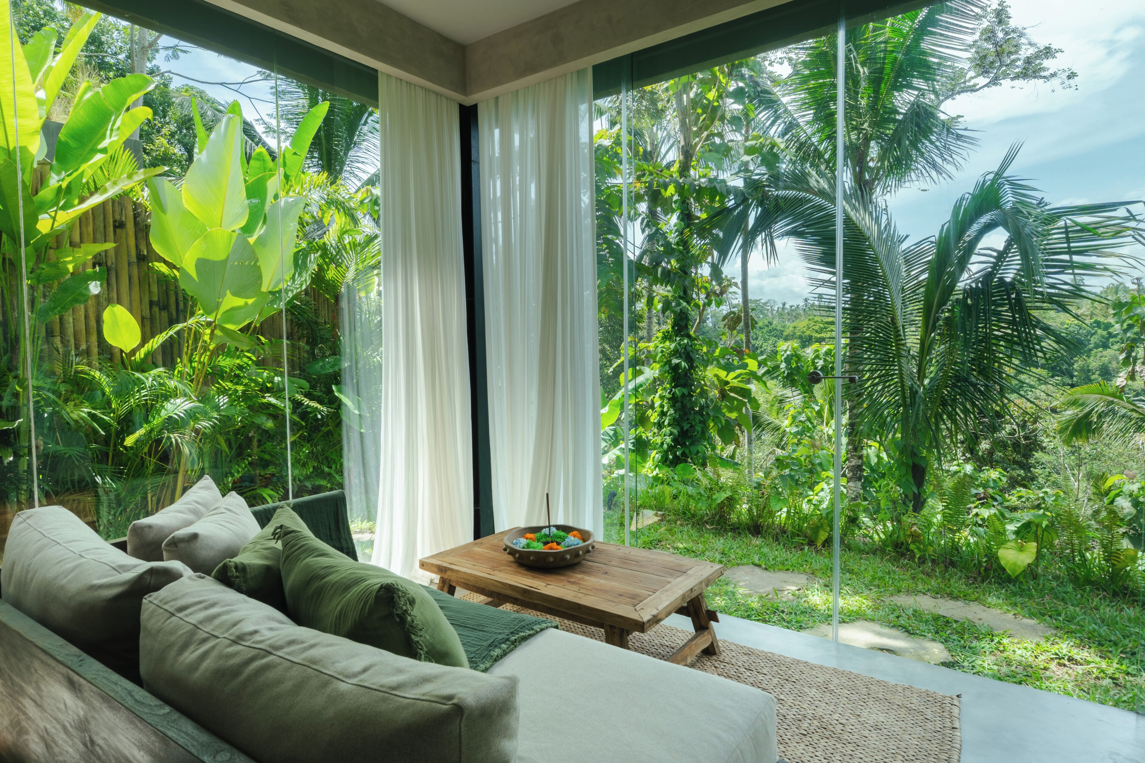 A room with a large window, a wooden coffee table, and a sofa with cushions.