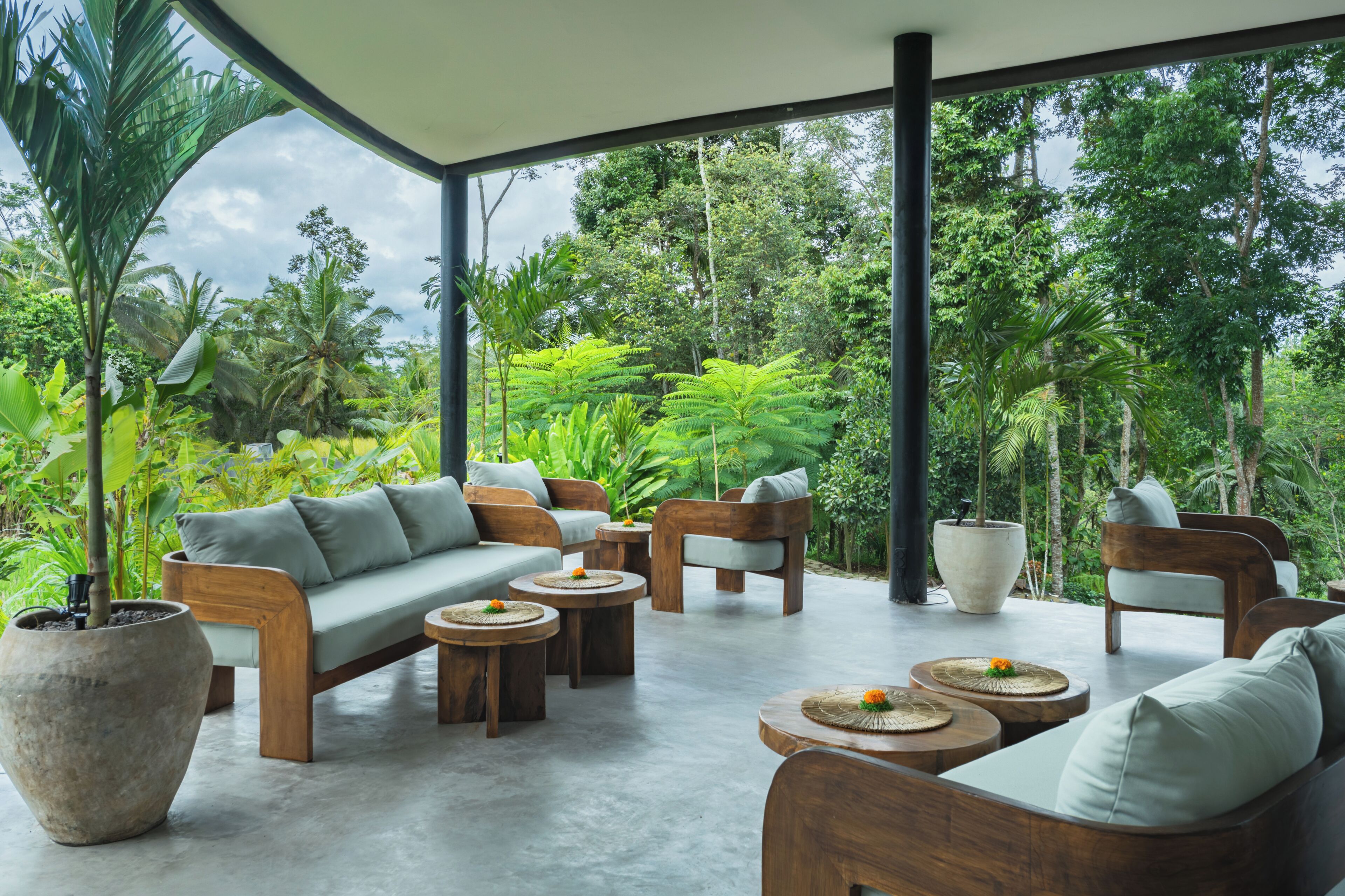 An outdoor seating area with wooden furniture and planters, surrounded by lush greenery.