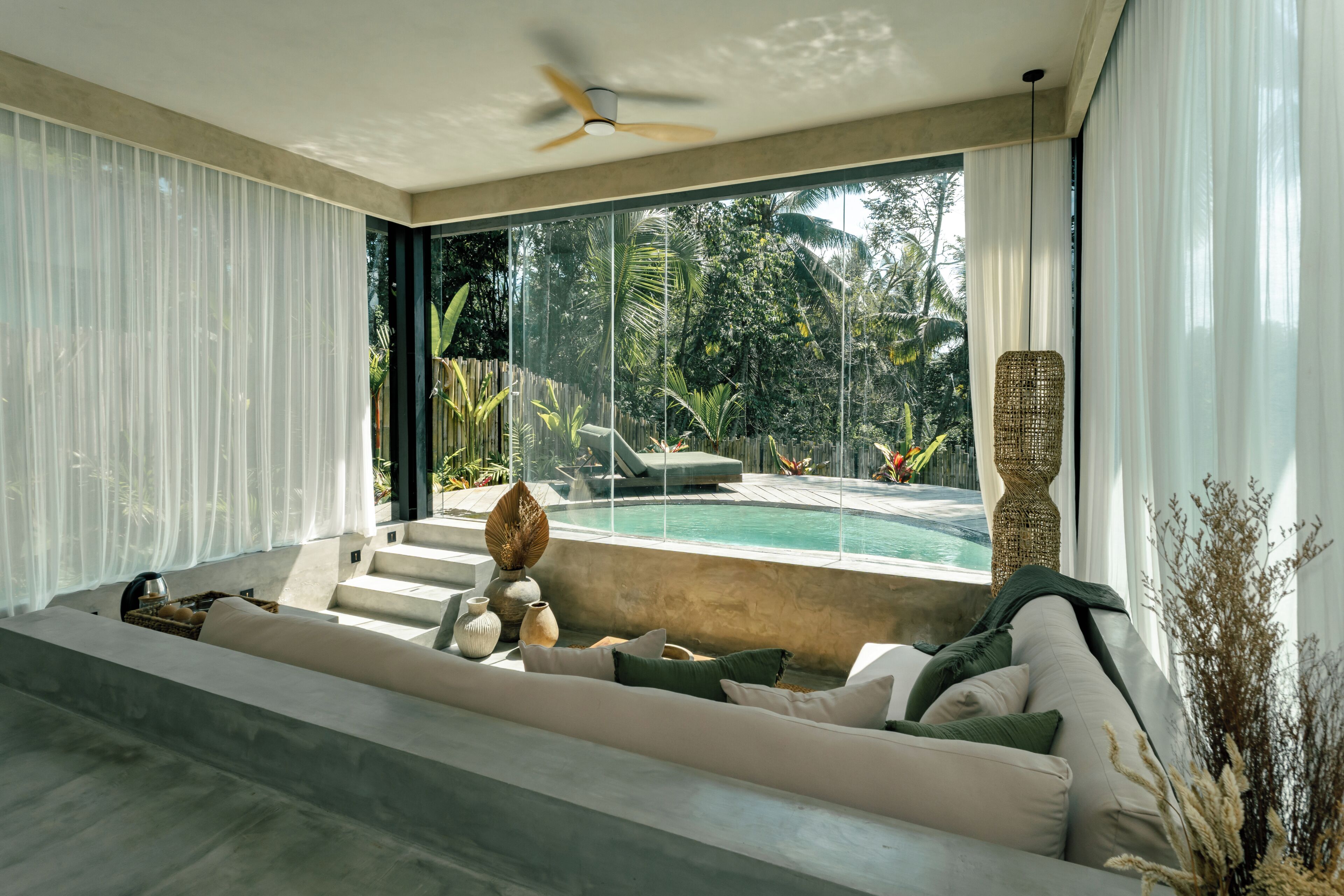 A modern living room with a large window, a ceiling fan, and a pool view.
