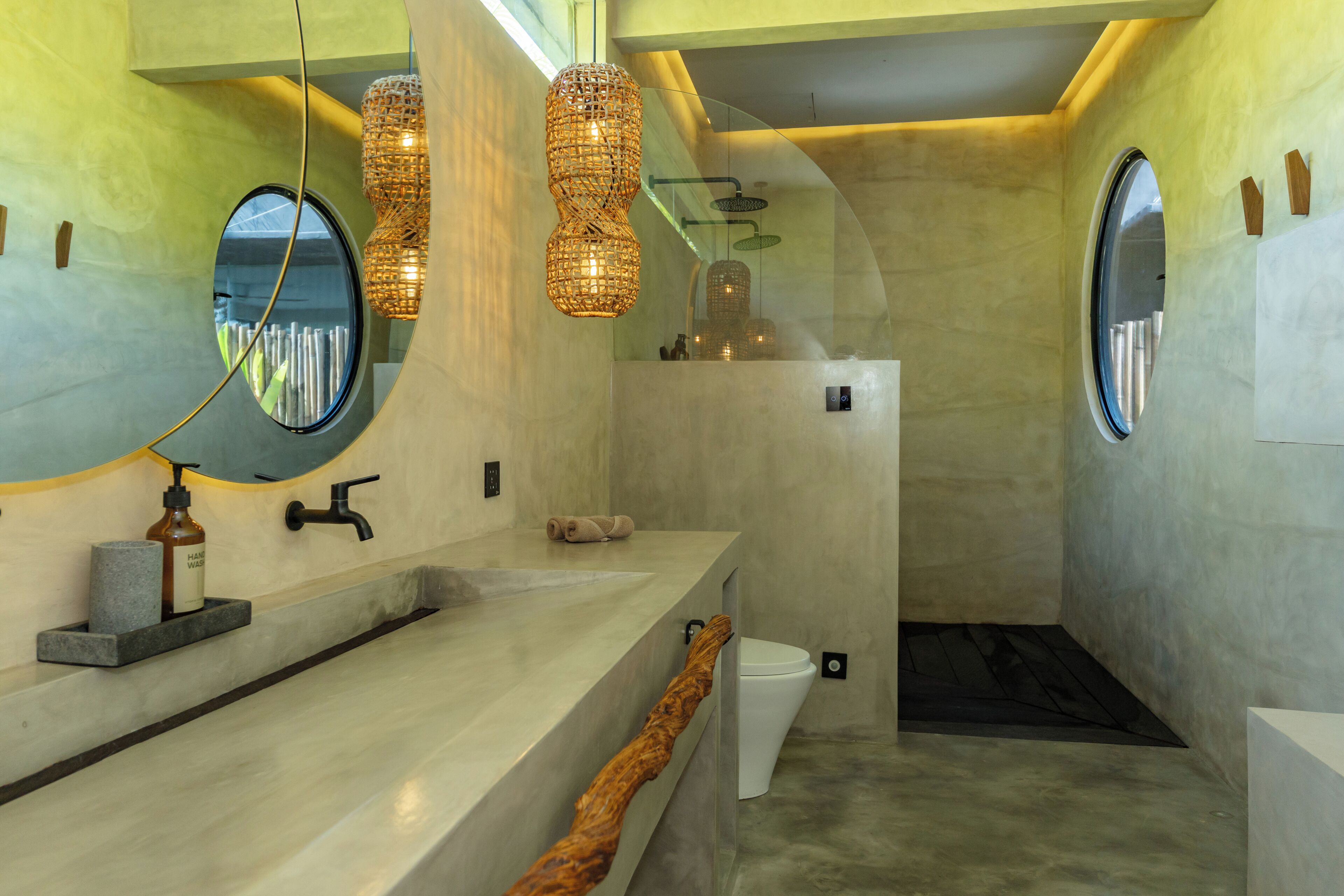 A modern bathroom with a large mirror, two pendant lights, a built-in sink, and a shower area.