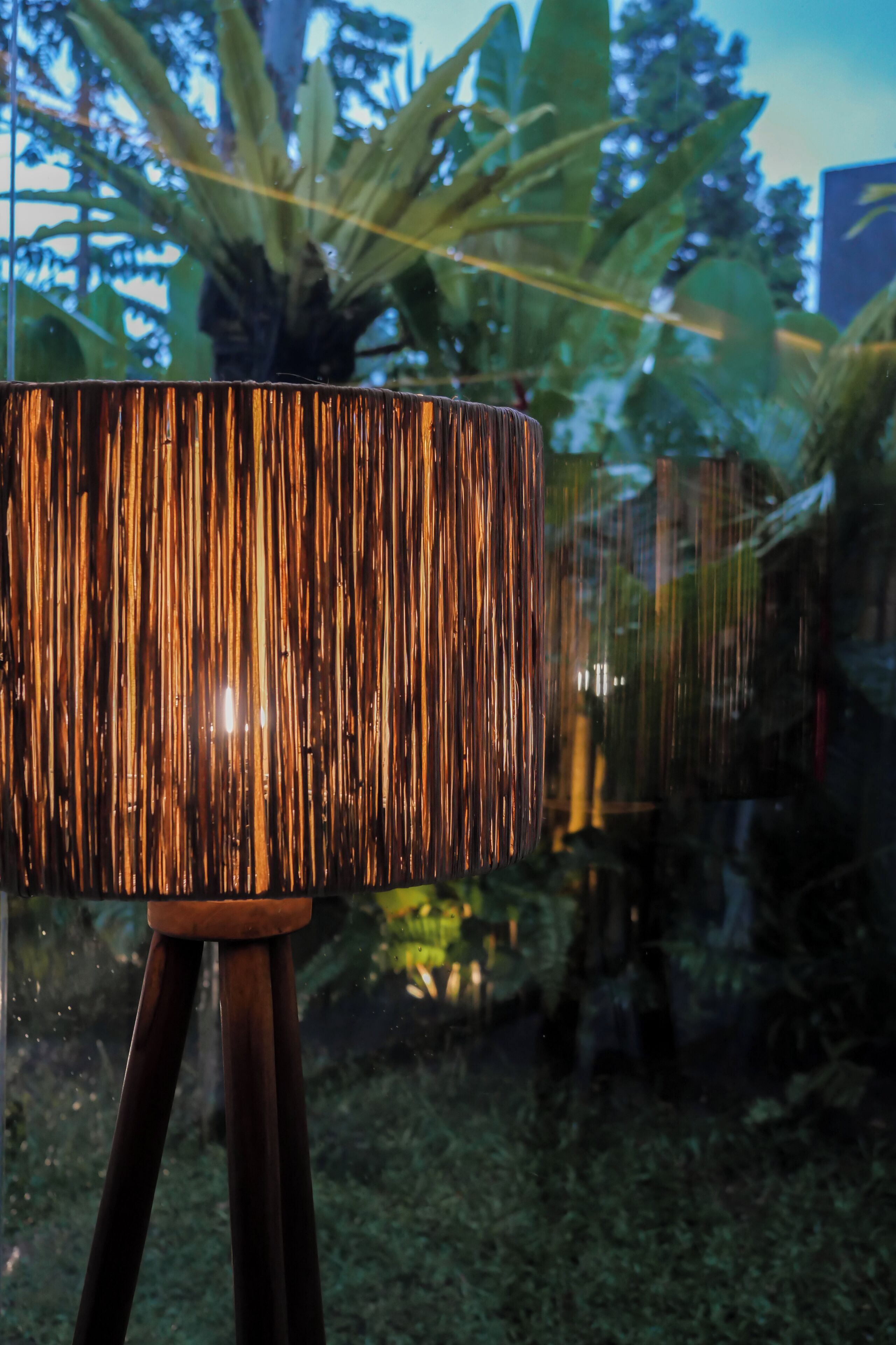 En lampe med en struktureret overflade på et tripod stativ, foran et grønt baggrund og et sløret bybillede.