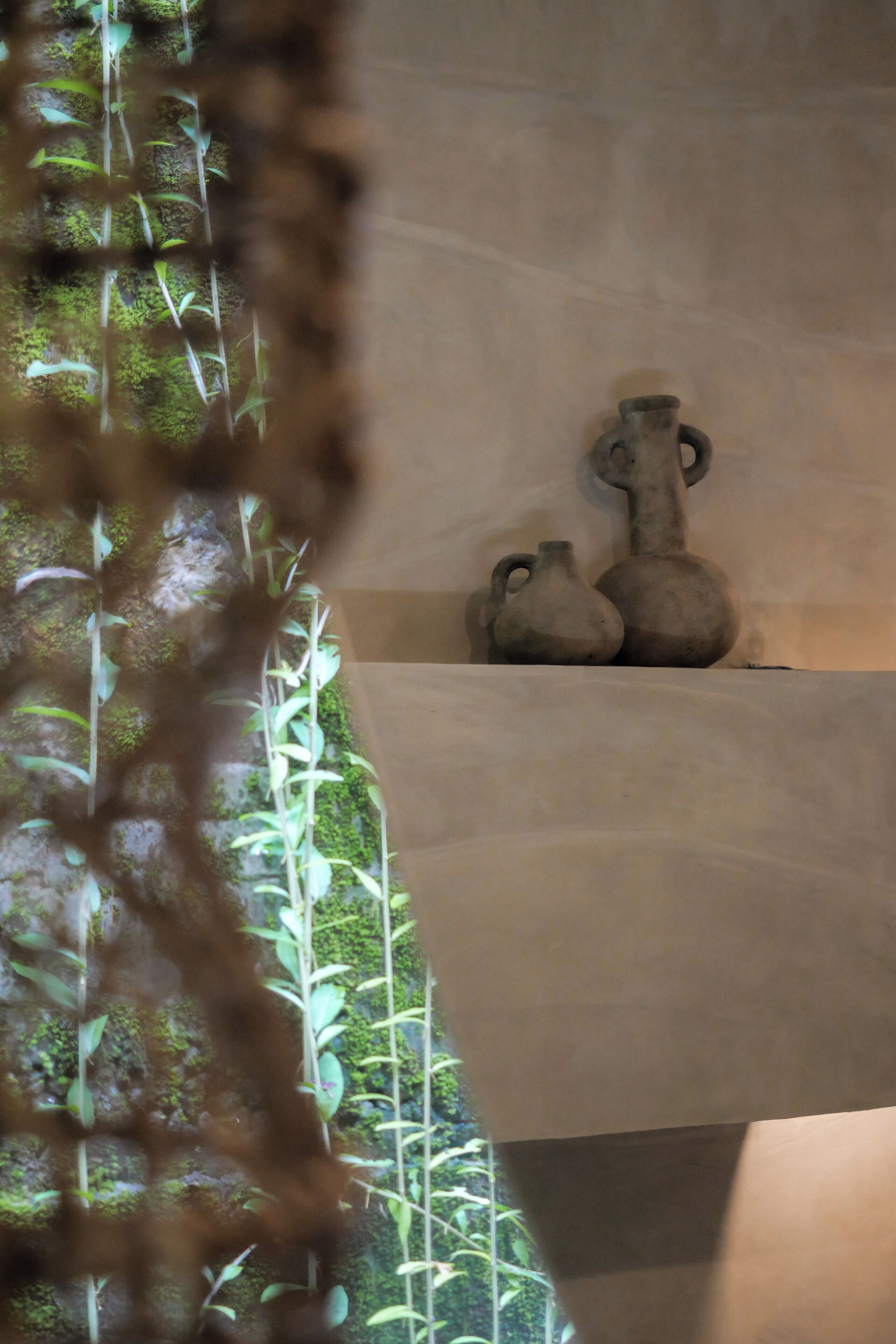 A room with a moss-covered wall, a small window, and two rustic vases on a shelf.