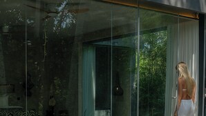 Un área de piscina moderna con paredes de vidrio, un sofá y una mesa de comedor.