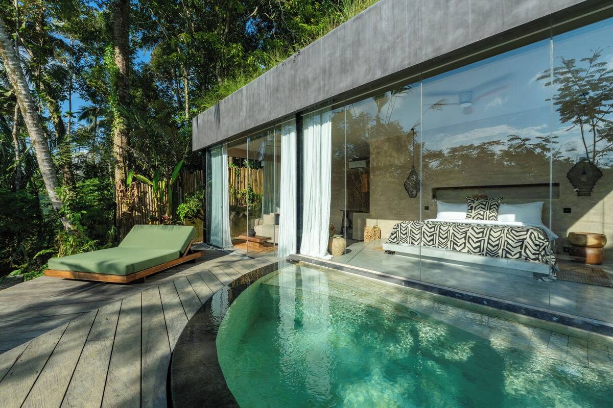 Una casa moderna con piscina, una silla de descanso y una cama con ropa de cama estampada.