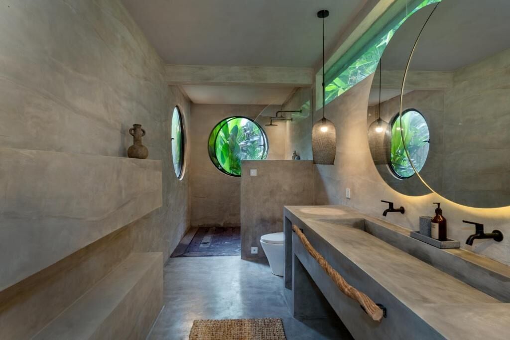 A modern bathroom with a large mirror, a wooden bench, and a circular window.