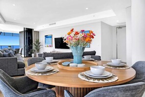 Ein moderner Essbereich mit einem runden Holztisch, grau gepolsterten Stühlen und einer blauen Vase mit Blumen.