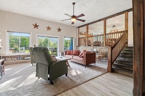 Ein geräumiges Wohnzimmer mit großem Fenster, Deckenventilator und Treppe zu einer oberen Ebene.