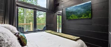 A bedroom with a large bed, a window with a view of trees, and a mounted picture on the wall.