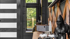 A room with a wooden door, a view of a deck, and a table with various items including a black sculpture. - Couples Retreat–2 Private Cabins,Hot Tubs,Firepits (Sevierville)