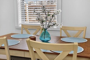 Ein Esstisch mit einer Vase weißer Blumen, Holzsesseln und blauen Platzsets.