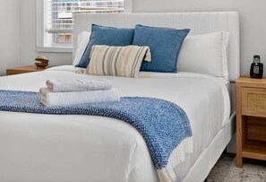 Ein ordentlich bezogenes Bett mit blauer und weißer Decke, einem weißen Kopfteil und einem Nachttisch mit Telefon.