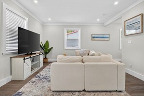 Ein Wohnzimmer mit einem Ecksofa, einem Flachbildfernseher, einer Topfpflanze und Kunstwerken an den Wänden.