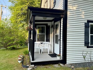 Une maison avec un porche, des chaises blanches et des plantes en pot.