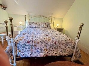 Une chambre à coucher avec une couvre-lit à motifs floraux, un cadre de lit en métal blanc, des tables de chevet avec des lampes et un fauteuil.