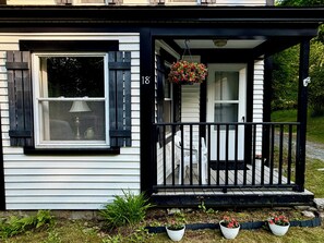 Une maison avec un porche, une jardiniÚre suspendue et le numéro 18 sur la porte.