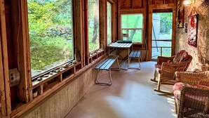 En rustik stuga med stora fönster, synliga träbjälkar, ett picknickbord, möbler av rotting och en vägg av sten.