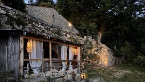 A rustic stone building with a wooden porch, stone walls, and a stone pathway leading to it.