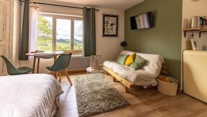 A bedroom with a bed, a sofa, a table, chairs, a TV, and a view of the outdoors.