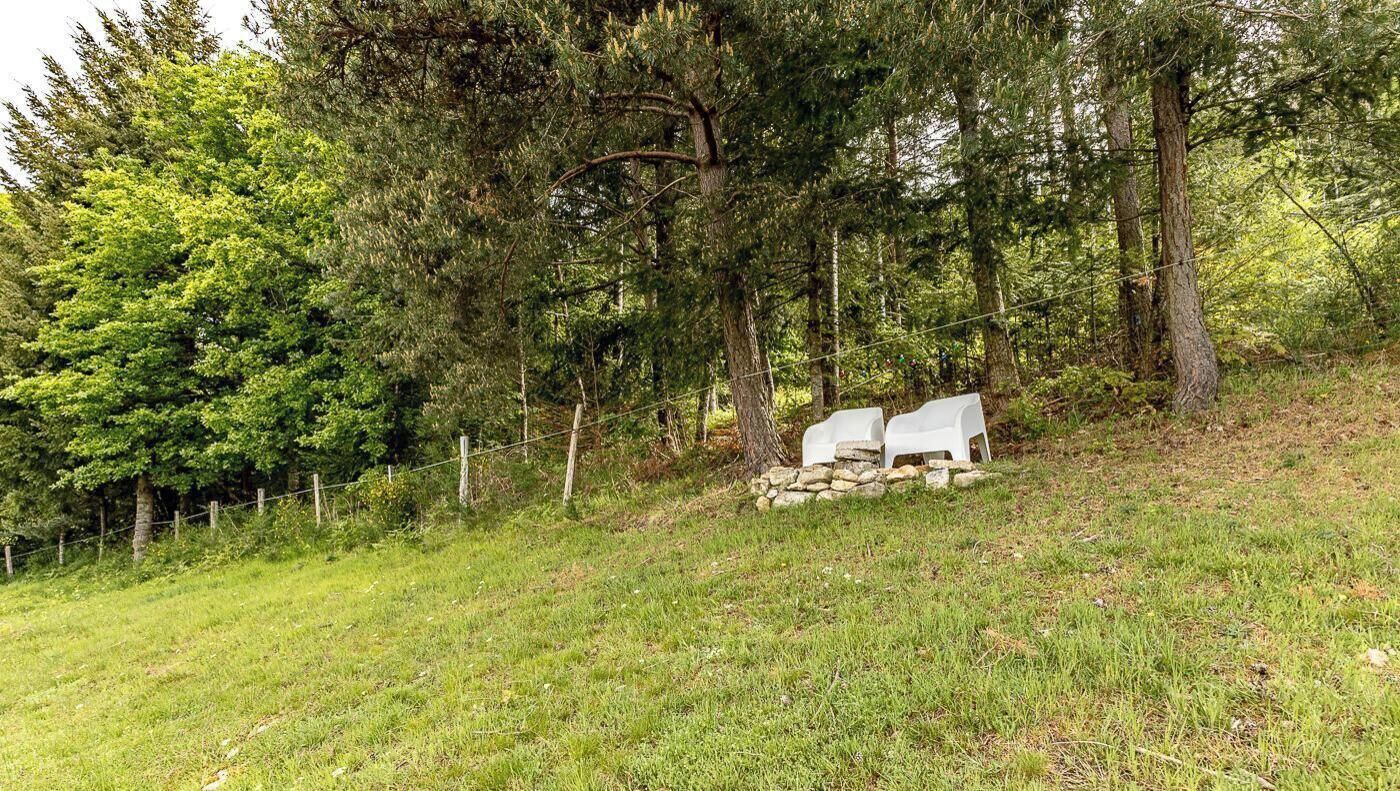 Uma área gramada ao ar livre com um muro de pedra e duas cadeiras brancas.