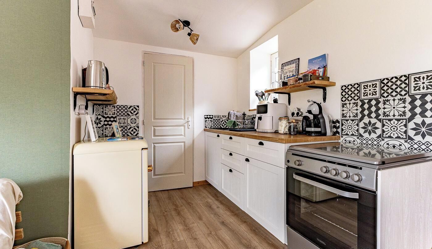 A compact kitchen with white cabinets, a wooden countertop, a stove, and patterned backsplash tiles.