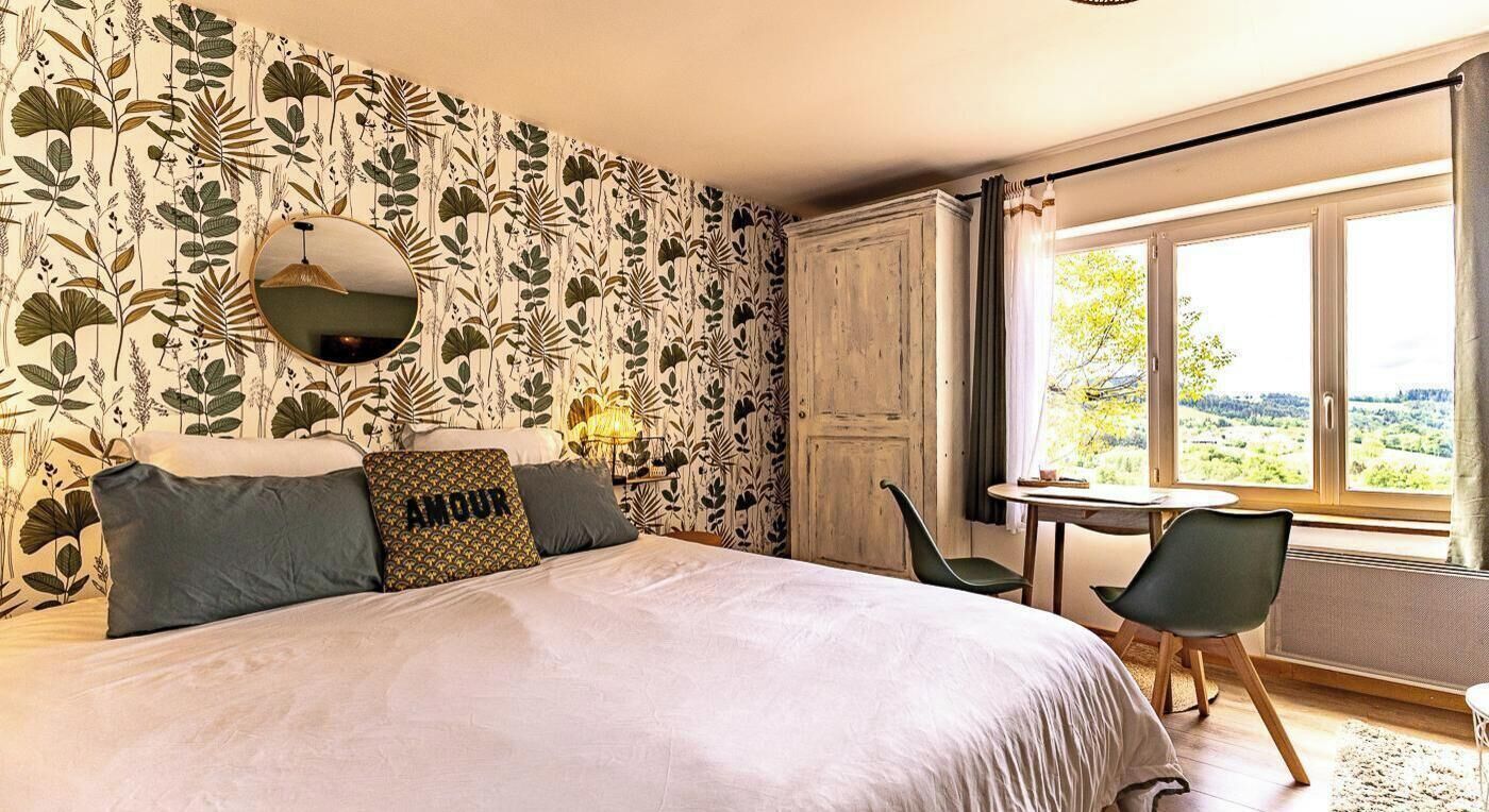 Ein Schlafzimmer mit einem großen Bett, einem runden Spiegel, einem kleinen Tisch, zwei Stühlen und einem Fenster mit Blick.