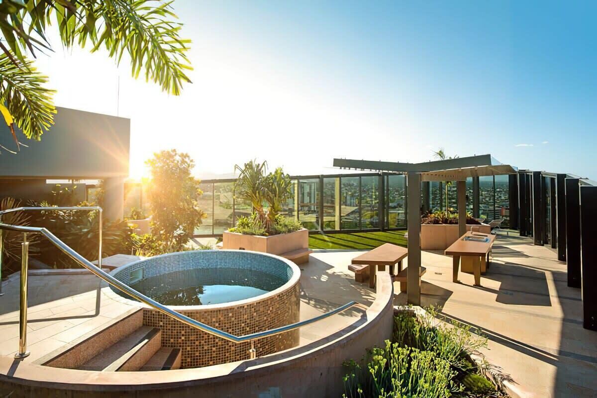 A rooftop pool area with a hot tub, outdoor seating, and a glass-enclosed space.