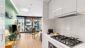 Una cocina moderna con estufa a gas, un comedor con mesa y sillas, y vistas de la ciudad a través de amplios ventanales.