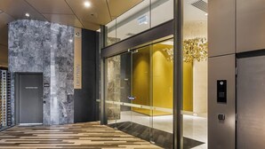 Un vestíbulo de ascensor moderno con pared de mármol, puerta de cristal y suelo de madera.