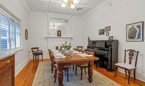 Ein Esszimmer mit einem Holztisch, gedeckt für sechs Personen, mit Stühlen, einem Kamin, einem Klavier und gerahmten Bildern an den Wänden.