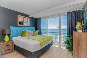 A bedroom with a bed, a nightstand, a lamp, a mirror, a window with a view of the sea, and a balcony. - Yachtsman S703A Studio (Myrtle Beach)