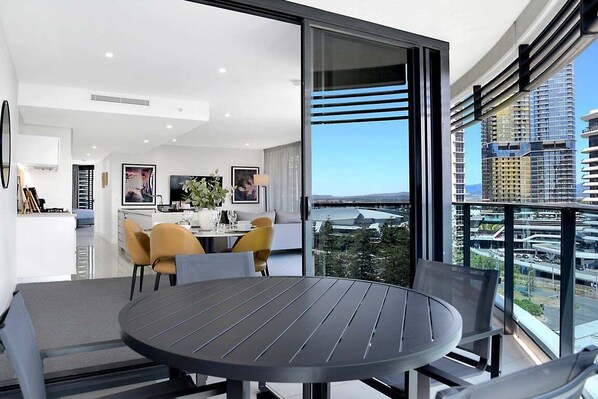 A modern apartment with a dining area, kitchen, and large windows offering city views. - Coastal Vibe at Oracle Level 10 (Gold Coast)