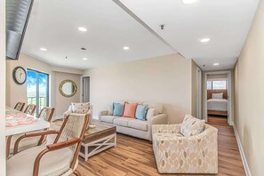 A spacious living area with a dining table, chairs, a sofa, and a patterned ottoman. - Ocean View 2BR Retreat-Renaissance Tower 1616 (Myrtle Beach)