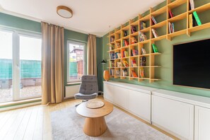 Ein Wohnzimmer mit Bücherregal, rundem Tisch, Stuhl und großem Fenster.