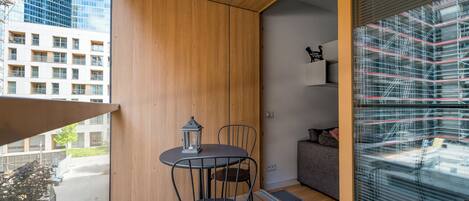 Un balcón con suelo de madera, una mesa con sillas, un farol y un sofá.